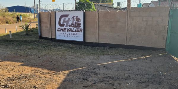 Signboard of Chevalier Haulage Limited on a wall topped with barbed wire.
