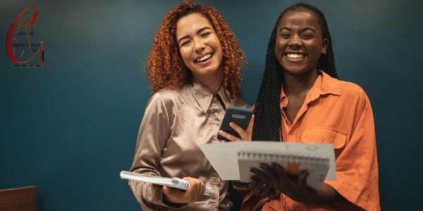 Two women smiling and holding notebooks in a casual setting.