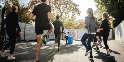 Group of people exercising outdoors, lifting one leg in unison.