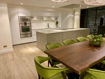 Modern kitchen with concrete island and green velvet chairs.