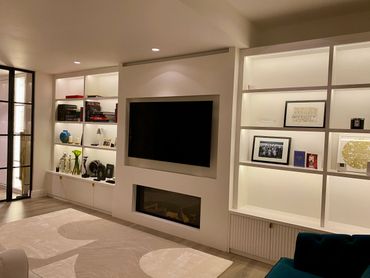 Modern living room with built-in shelves, TV, and fireplace.