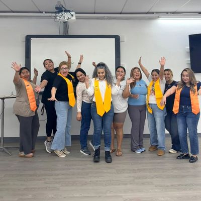 Group of women celebrating with yellow scarves in a classroom.