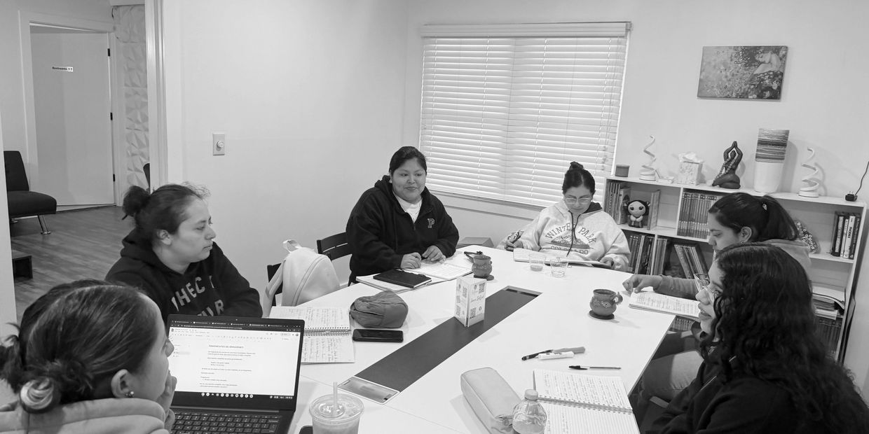 A group of people engaged in a GED class around a table with notebooks and laptops.