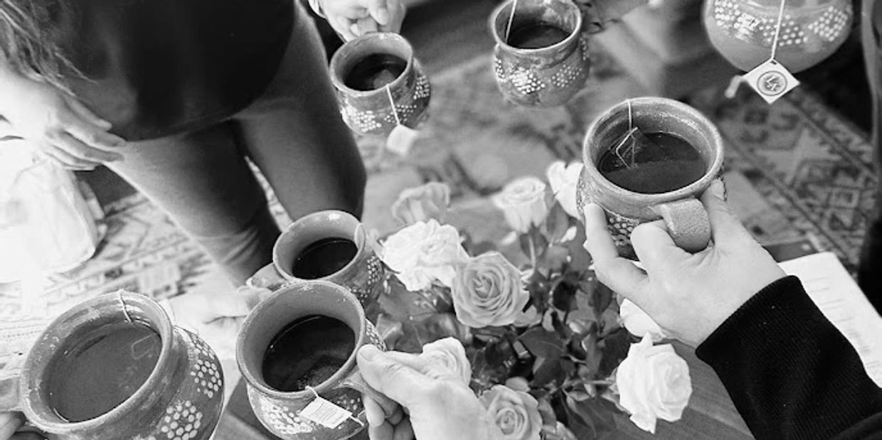 People holding cups of tea around a table with roses.
