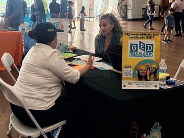Two women chatting at a GED Trailblazers info table.
