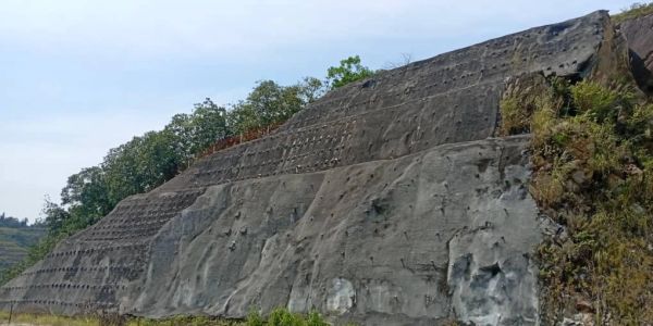 Large concrete retaining wall on a hillside with vegetation.