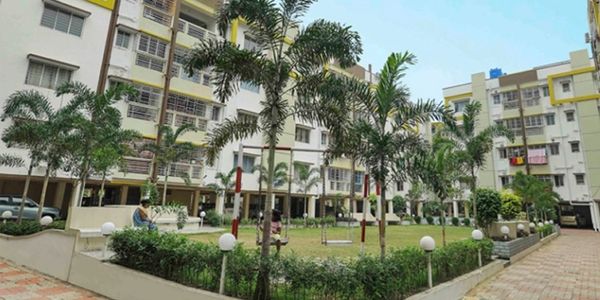 Residential complex with green courtyard and palm trees under clear sky.