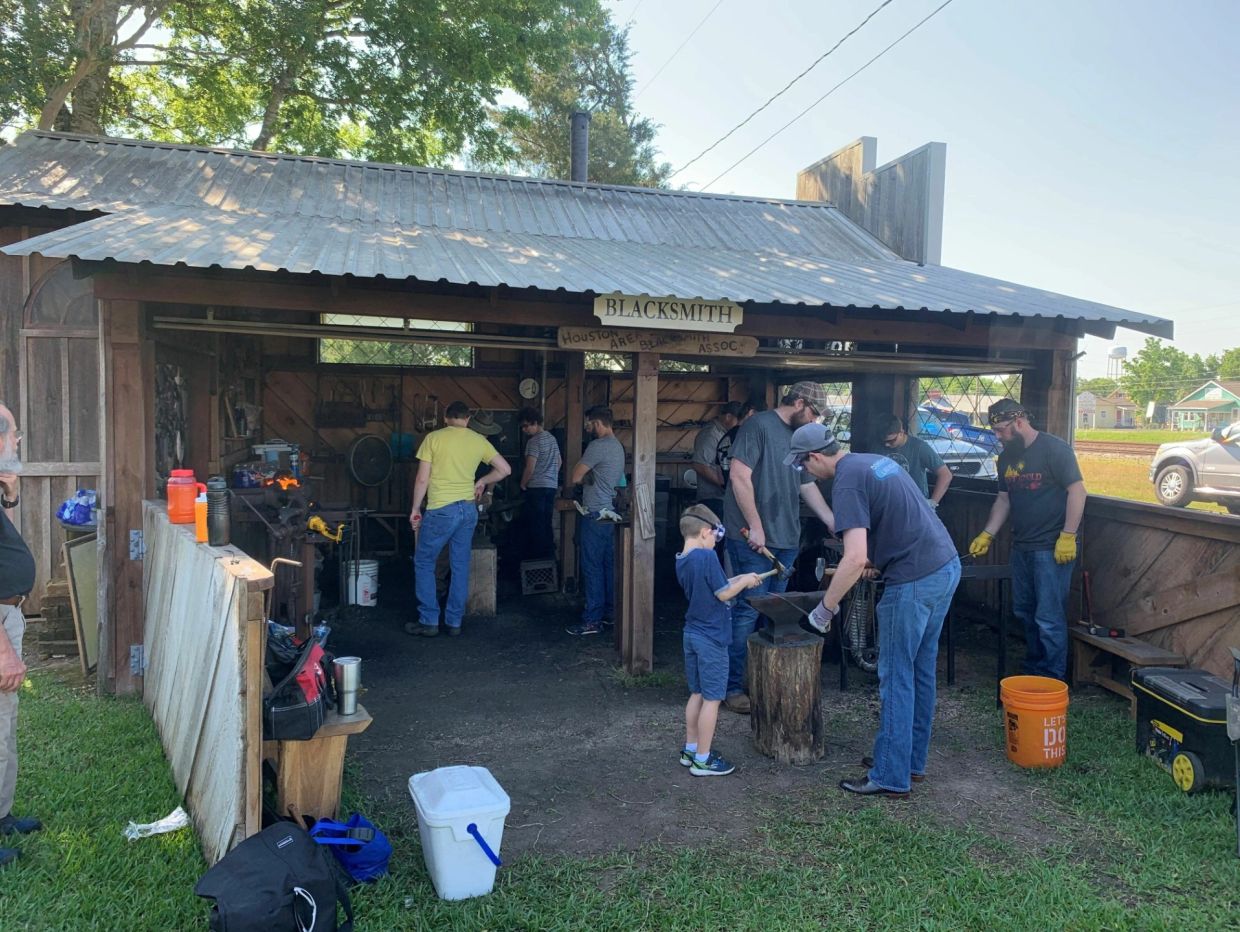 People learning blacksmithing in an outdoor workshop.