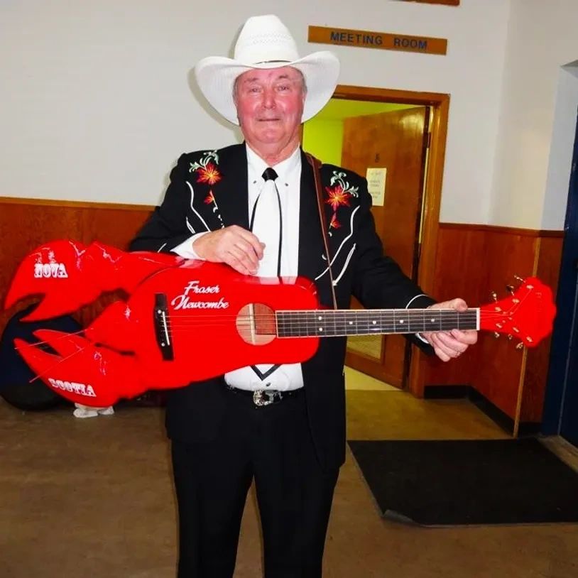 Man in cowboy hat holding a red lobster-shaped guitar.