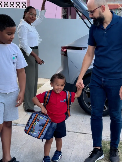 Family preparing for school with backpacks near a car.
