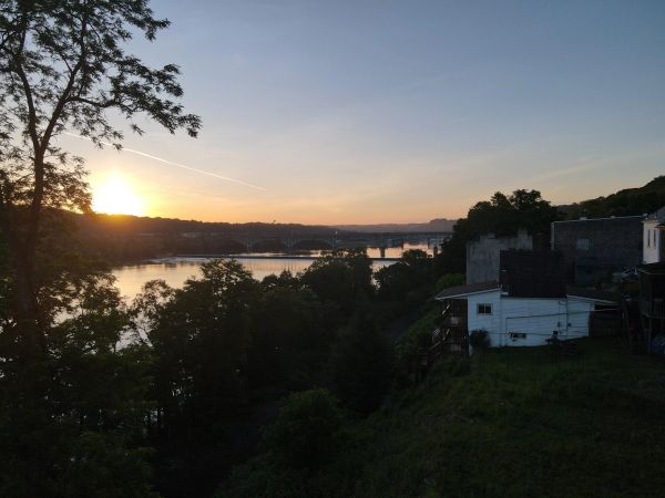 Sunset over a river with trees and houses along the shore.