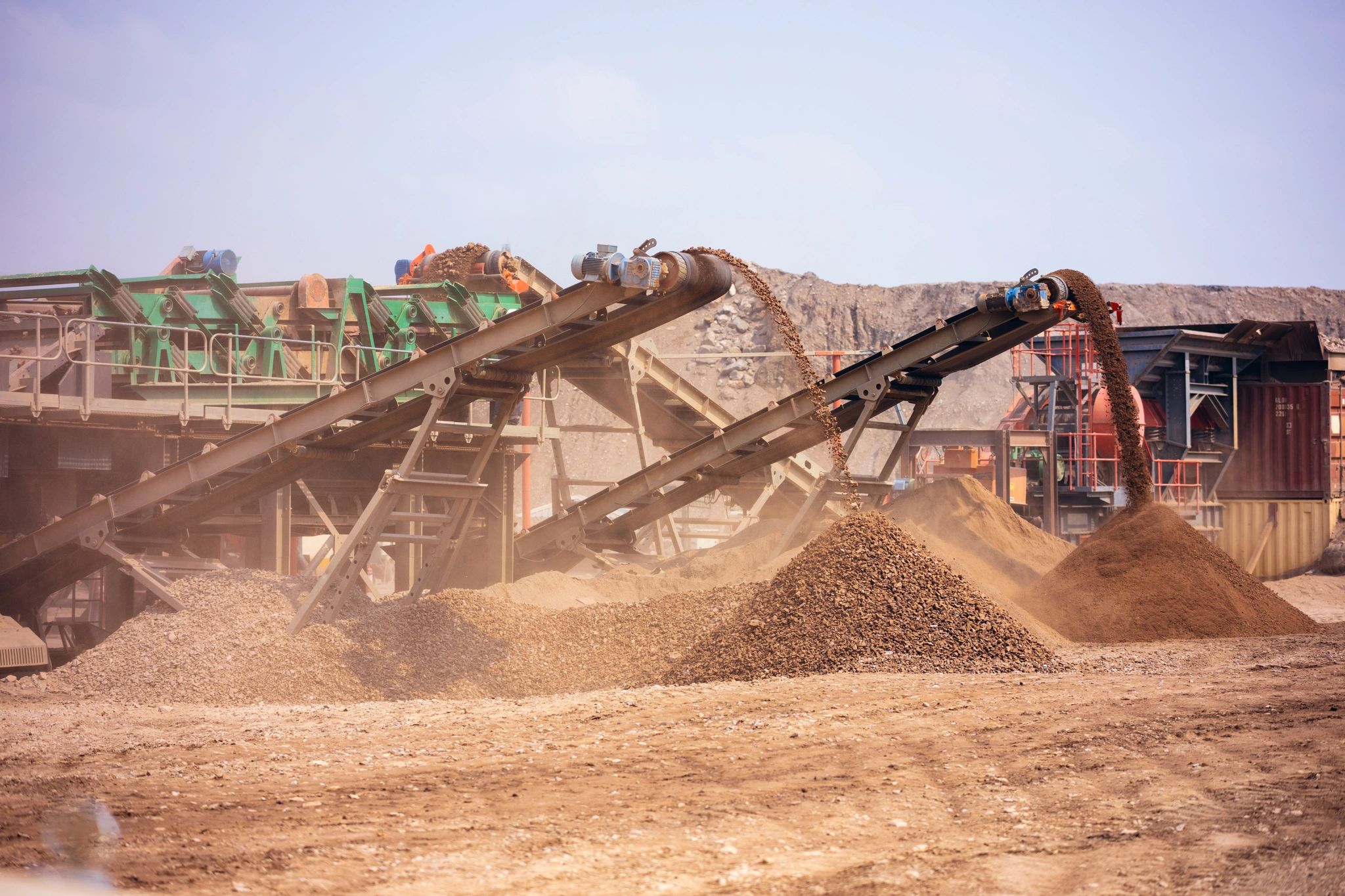 Industrial conveyor belts sorting and piling gravel at a mining site.