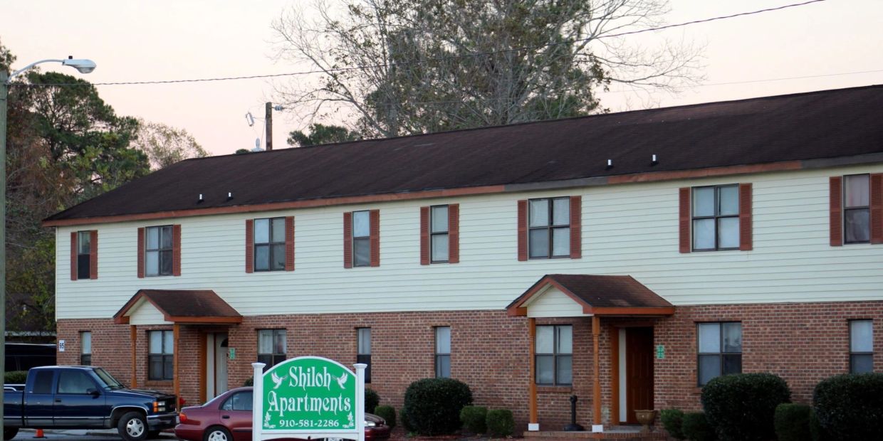 Shiloh Apartments building with parked cars and a green sign in front.