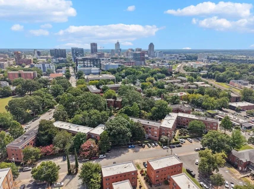Aerial view of a cityscape blending urban buildings with abundant greenery under a blue sky.