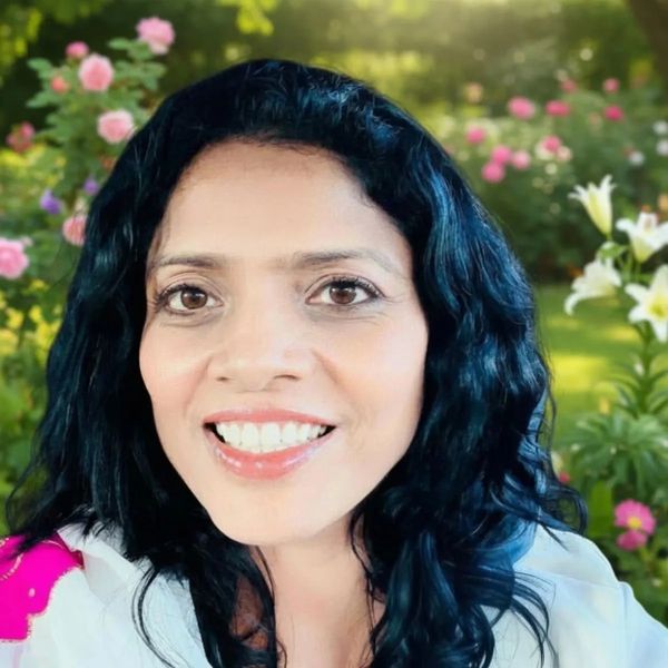 Smiling woman with dark curly hair in a garden.