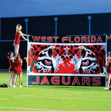 Cheerleaders hold a West Florida Jaguars banner on a football field.