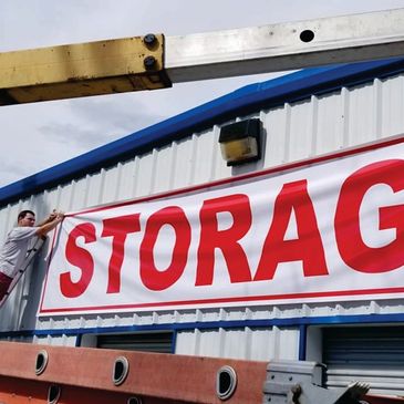 Worker installing a large storage sign on a building exterior.