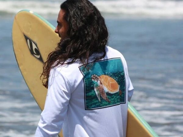man with a white upf shirt with a turtle on it and a surfboard.