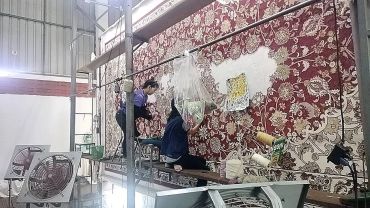 คนสองคนกำลังทำงานบนพรมลายดอกไม้ใหญ่