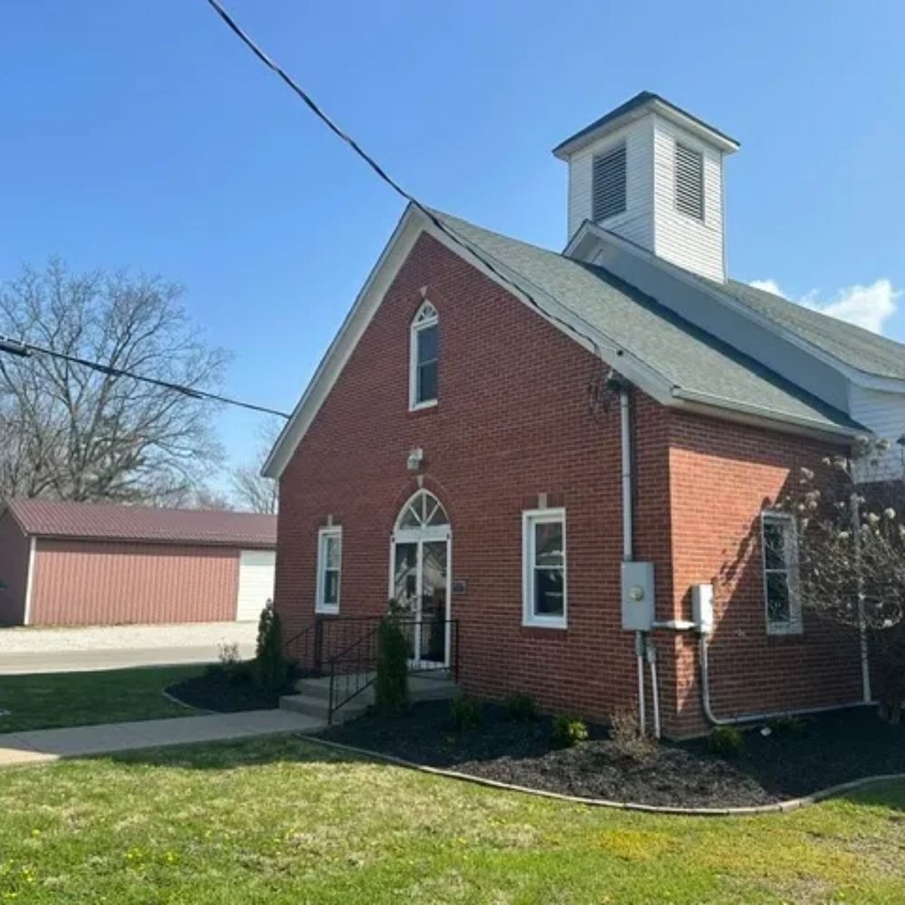 Small brick church with white steeple under clear blue sky.
