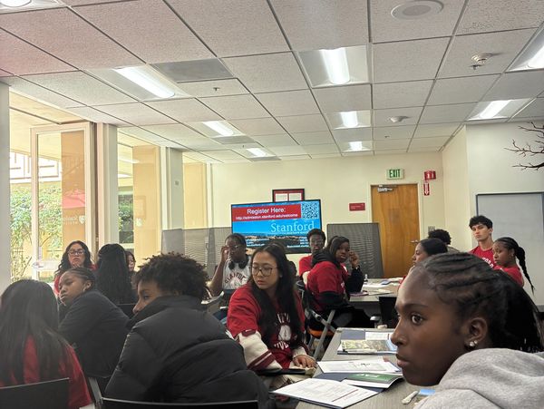 Students attentively participating in a classroom setting with a Stanford registration sign in the background.