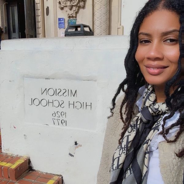A woman smiling next to a Mission High School sign on a white wall.