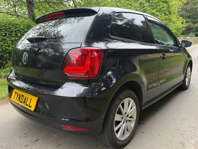 Black Volkswagen hatchback parked on a road surrounded by greenery.