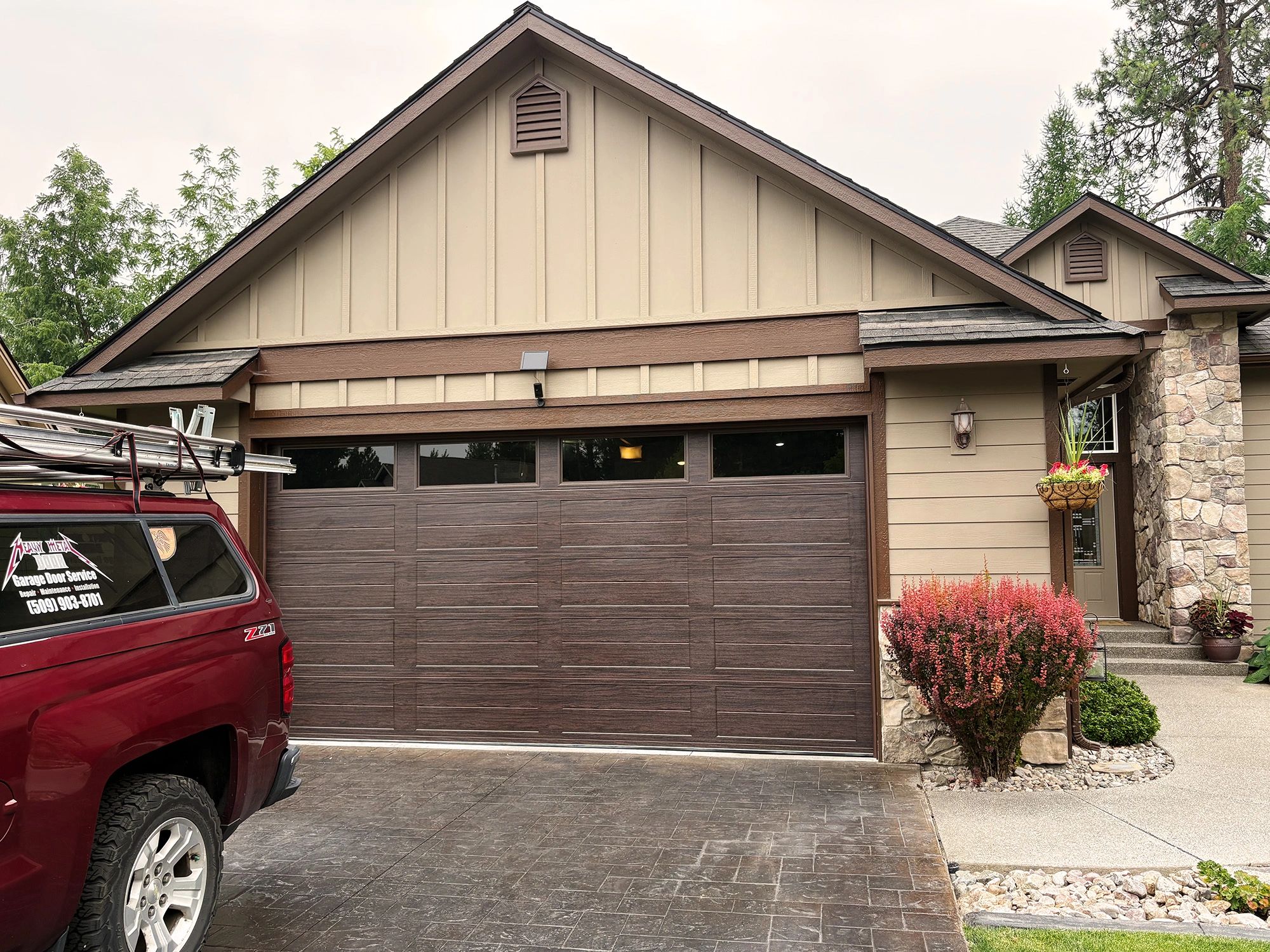 Heavy Metal Door service truck parked in front of a newly installed dark woodgrain residential garage door with top-panel windows in Spokane, WA.