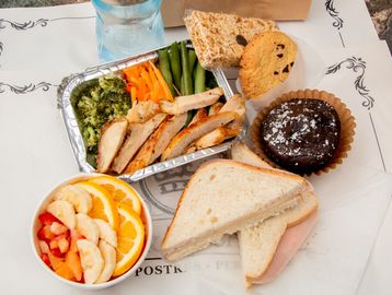 A meal with sandwich, salad, grilled chicken, vegetables, cookies, and a chocolate dessert.