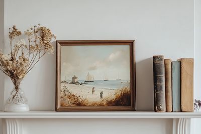 A mantle piece with a vase, artwork and books