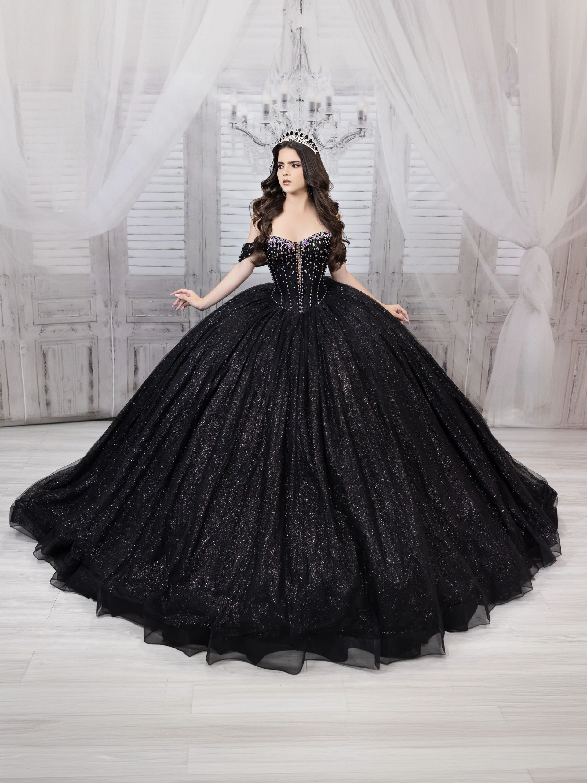 Woman in a sparkling black ball gown and crown poses elegantly indoors.