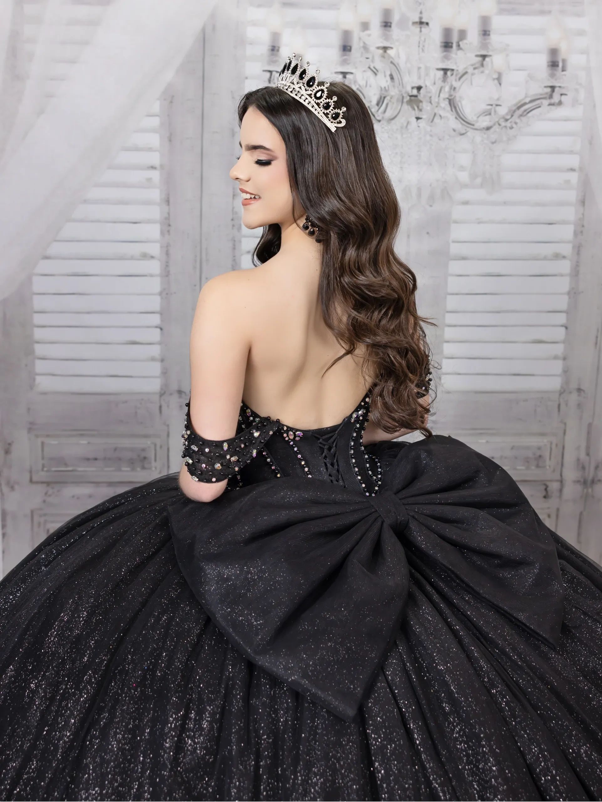Young woman in elegant black ball gown and tiara, smiling gracefully.