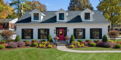 Charming suburban house with a red door and colorful garden beds.
