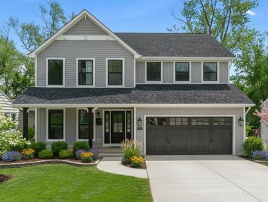 Two-story gray house with black garage doors and well-manicured lawn.