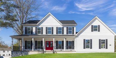 Traditional white two-story custom home with a wrap-around porch, black shutters, and signature red 
