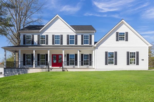 Large white house with black shutters and red front doors on a sunny day.