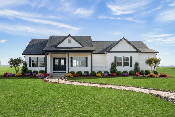 Modern white house with black roof and colorful flower beds.