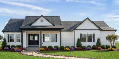 Modern white house with black roof and colorful flower beds.