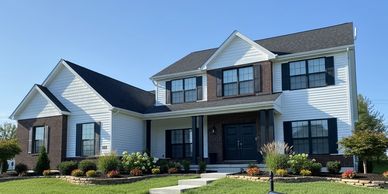 Large two-story house with brick and white siding, manicured lawn, and flower beds.