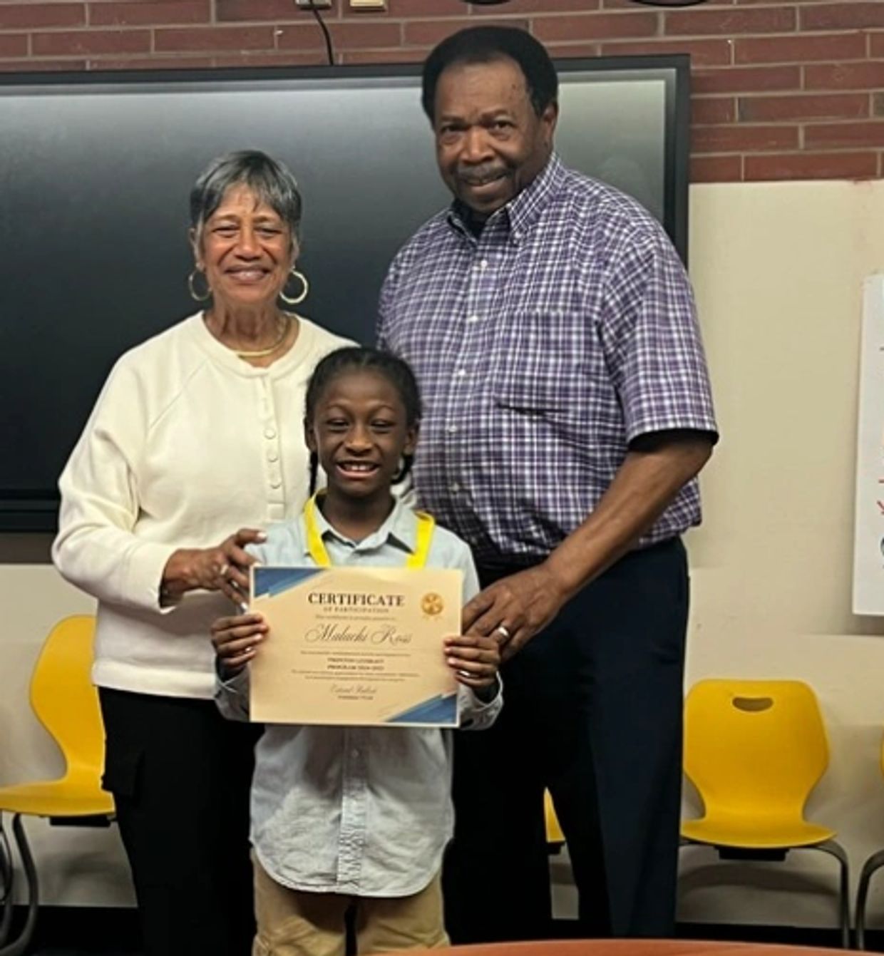 Young boy proudly holding a certificate with adults behind him.