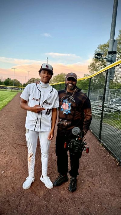 Two men posing on a baseball field, one in a baseball uniform.