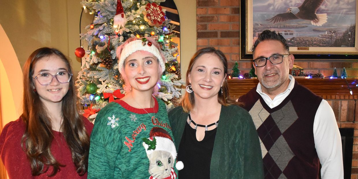 A festive family photo in front of a decorated Christmas tree and fireplace.