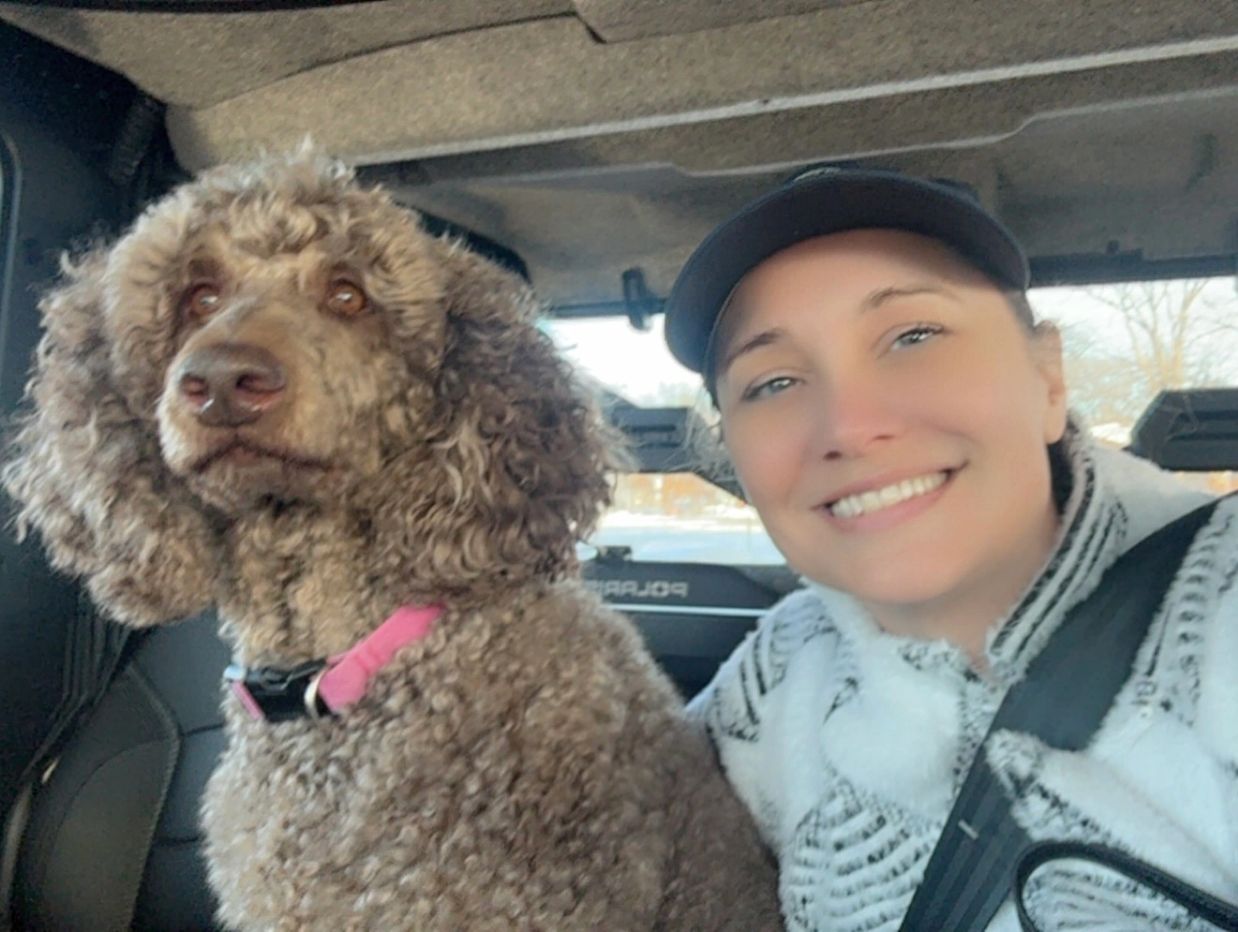 Woman and her brown standard poodle riding in a vehicle.