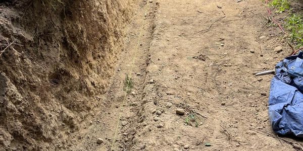 A dug trench along a dirt path with a blue tarp on the side.