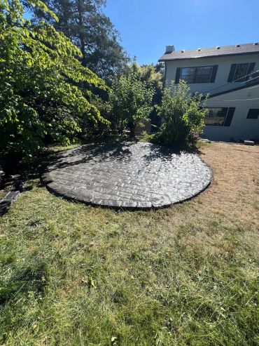 A circular stone patio in a sunny backyard with surrounding greenery.