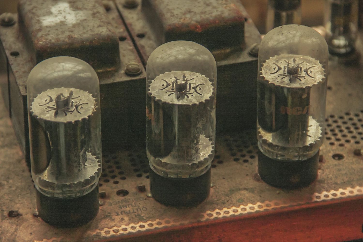 Three vintage vacuum tubes on a rusted metal base.
