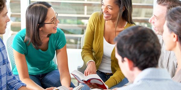 Group of young people smiling and discussing with books in hand.