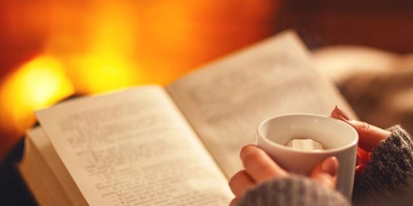Cozy scene with hands holding a cup and an open book by warm light.