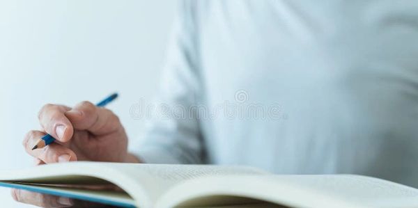 Person holding a pencil and reading an open book.