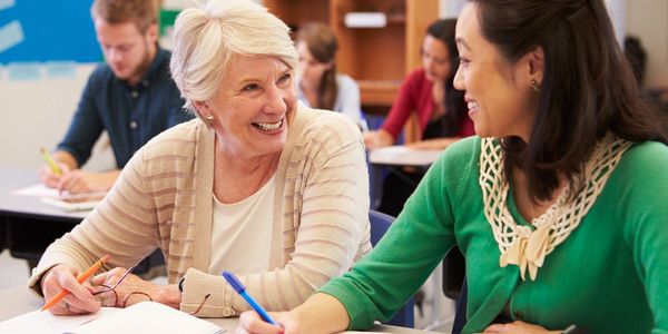 Two women smiling and interacting while studying in a classroom.